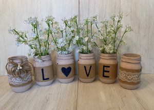 Four pink mason jars with the letters "L O V E" spelled out, one letter per jar